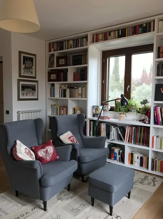 a reading space with bookcases that surround the window, graphite grey Strandmon chairs and an ottoman and a printed rug