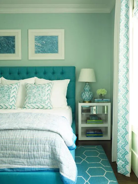 a retro inspired aqua bedroom with a turquoise upholstered bed and printed bedding and a rug, a nightstand with books