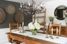a rustic dining room with planked walls, a gallery wlal of baskets, a stained table and chairs, a white bench and a catchy chandelier