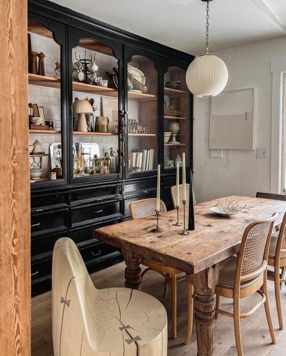 a rustic vintage dining room with a large black buffet with decor and dishes, a vintage stained table and rattan and wood chairs