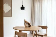 a simple and minimal dining space with a stained table and chairs, a black pendant lamp and a piece of rock for an accent