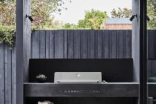 a small minimalist grill area with a large black concrete unit with a built-in grill and some firewood underneath