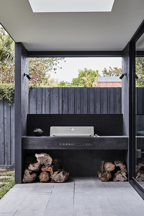 a small minimalist grill area with a large black concrete unit with a built-in grill and some firewood underneath
