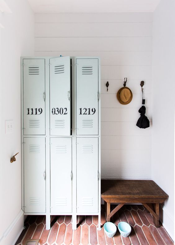 a small mudroom with a skinny tile floor, light blue metal lockers with numbers, a stained bench and some decor