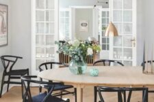 a stylish Scandinavian dining room with a light-stained oval table and black wishbone chairs, elegant copper pendant lamps