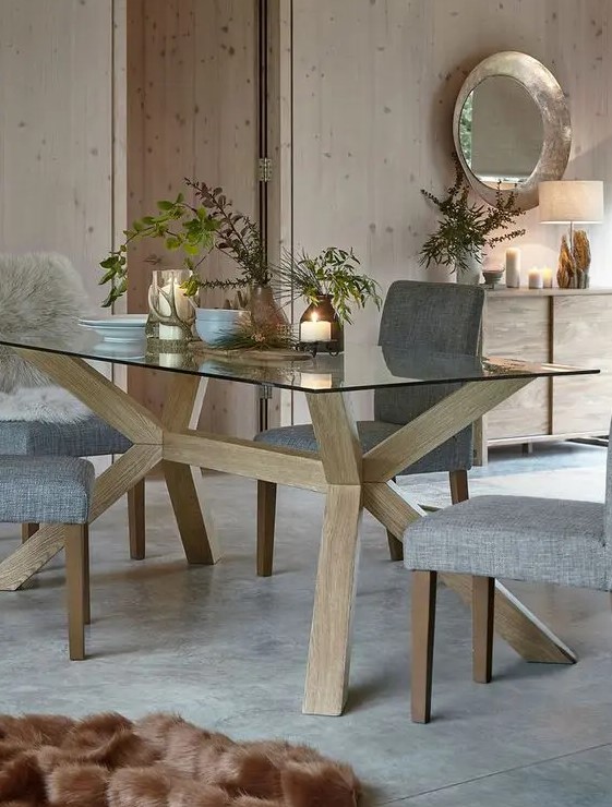 a stylish Scandinavian dining table with a glass tabletop and wooden legs holding it, with grey chairs for a peaceful dining zone