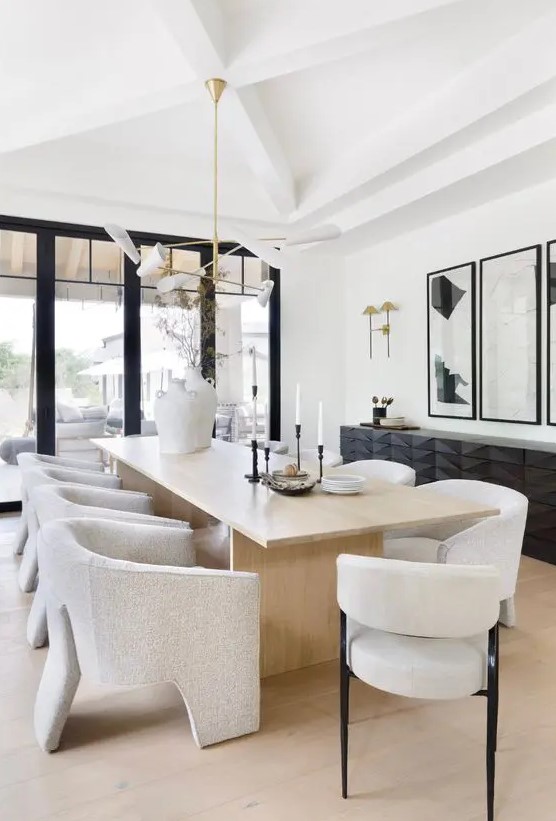 a stylish and refined minimalist dining space with a black sculptural console, a light stained table and neutral chairs, a catchy chandelier