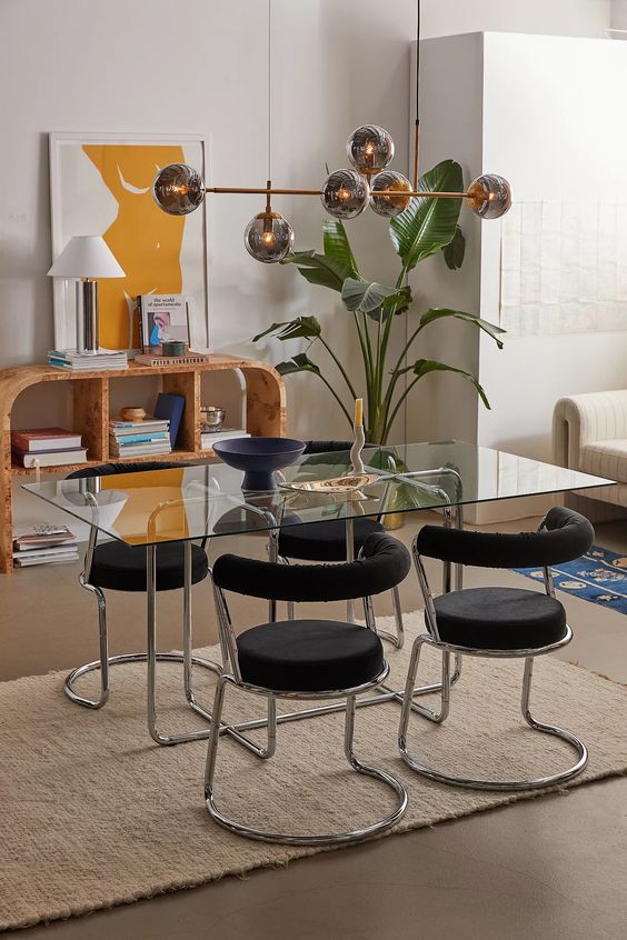 a stylish dining room with a glass top dining table and a metal piping base and matching black chairs, a bubble chandelier and a storage unit