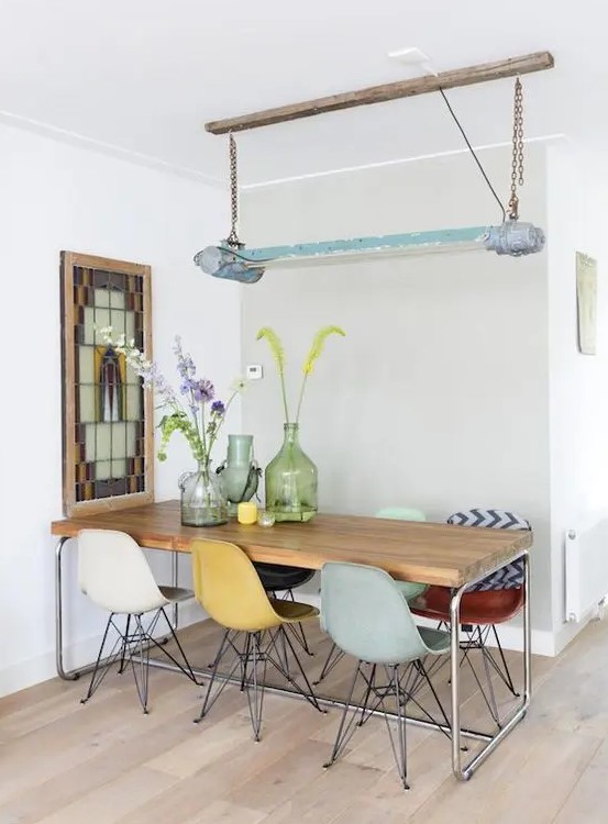 a stylish dining space with a long dining table, colorful Eames chairs, a mosaic artwork and a catchy lamp on chain
