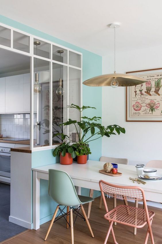 a stylish dining space with a turquoise accent wall, a white table, blush wire chairs and an aqua Eames one plus a pendant lamp