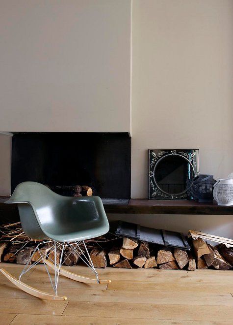 a stylish fireplace nook with firewood, a green Eames rocking chair and some decor is a cool space