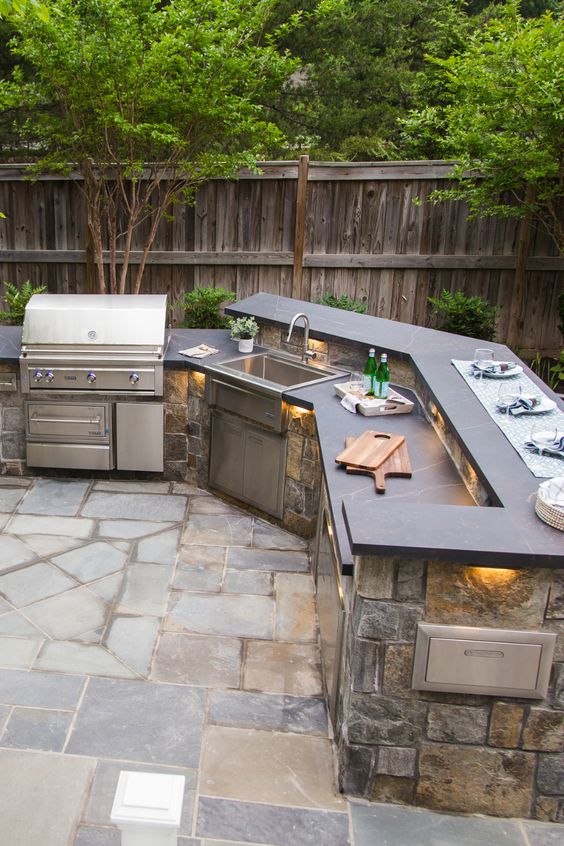 a stylish outdoor grill space with a large stone clad unit with a grill, a sink and some countertops for cooking is awesome