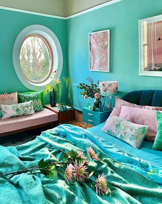 a super bright and quirky bedroom with turquoise walls, a radiator and a nightstand, an oval window, a pink daybed with colorful pillows, a black bed with bright turquoise and pink bedding