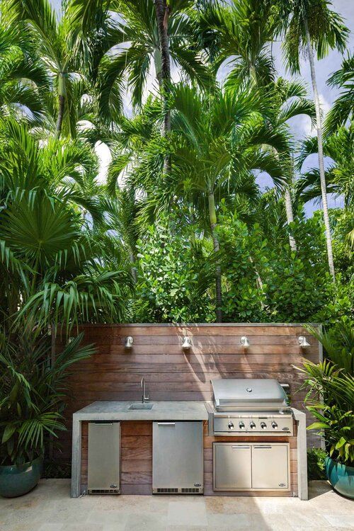 a tropical outdoor kitchen with a large concrete unit with a sink and a grill and lots of greenery around is perfect