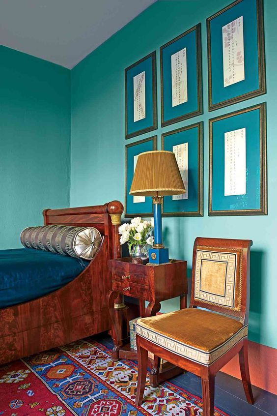 a vintage bedroom with turquoise walls, a rich-stained bed and a nightstand, a chair and a gallery wall