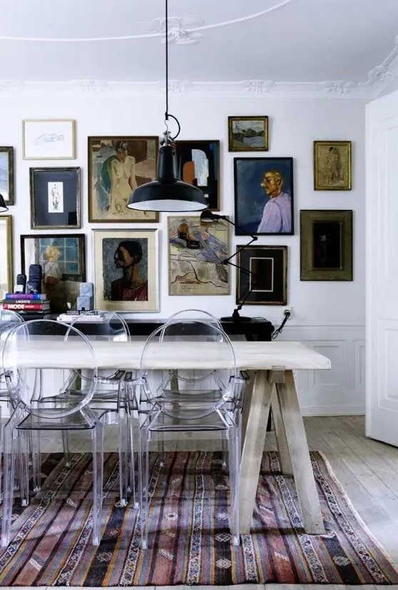 a vintage dining room with a trestle dining table, ghost chairs, a bold printed rug and a vintage gallery wall