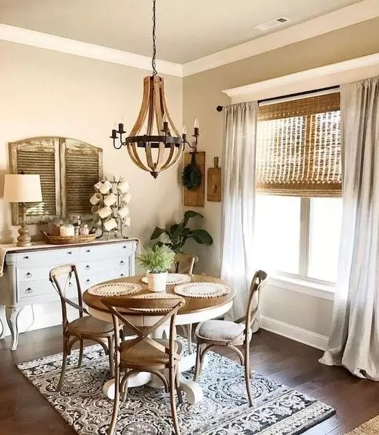 a vintage farmhouse dining area with wicker shades, a vintage wooden dining set, a white sideboard, shutters and a wooden chandelier