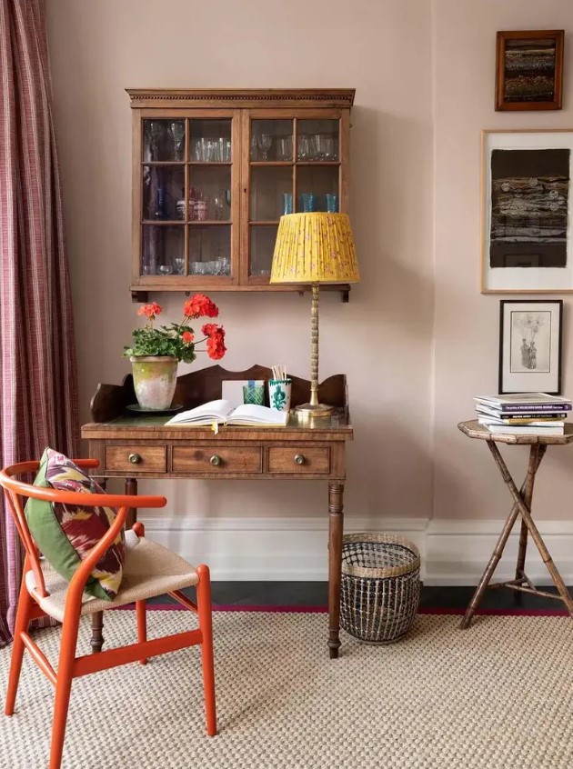 a vintage working space with a dark-stained desk and a cabinet, an orange wishbone chair and a side table, some art