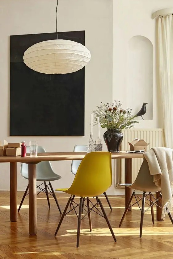 a welcoming dining space with a dining table and muted color Eames chairs, a paper pendant lamp and some dried flowers