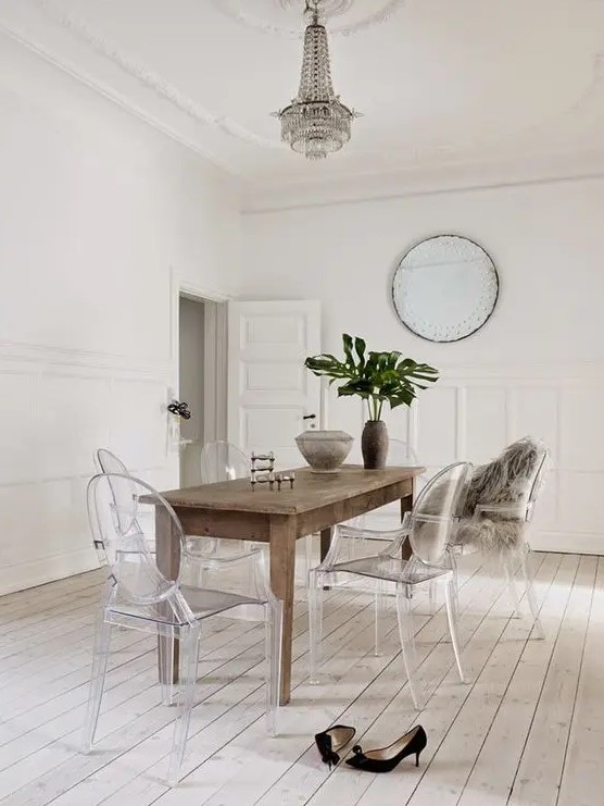 an airy dining room with a stained table, ghost chairs, a crystal chandelier and a round mirror plus statement leaves