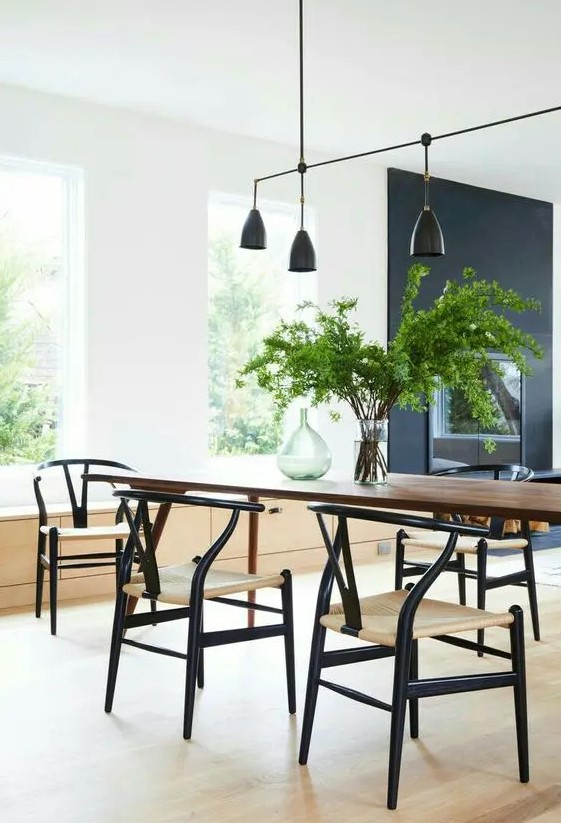 an airy dining space with a dark-stained table and black wishbone chairs, a catchy black pendant lamp over the table