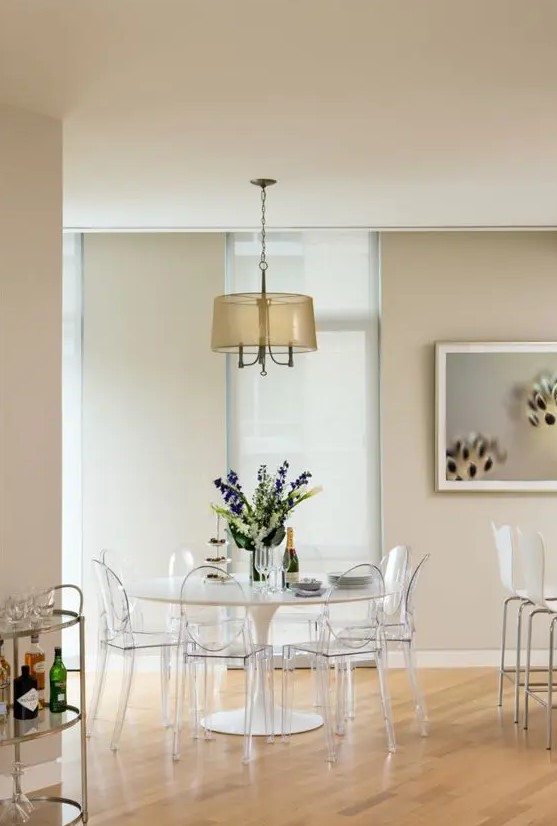 an airy dining space with a round table, ghost chairs, a pendant lamp and some art is a cool idea