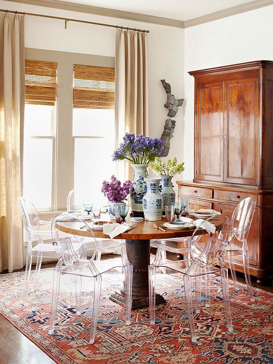 an eclectic dining space with a rich-stained table and a buffet, ghost chairs, a printed rug and layered window treatments