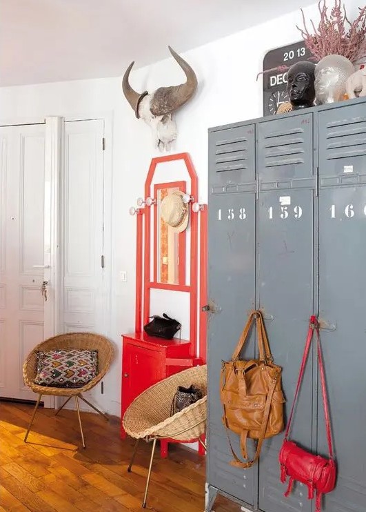 an eclectic space with grey metal lockers, a bold red console table, rattan chairs, bold bags and bright decor on top the lockers