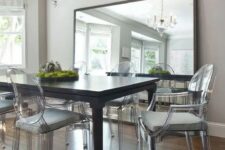 an elegant dining room with a black dining table, ghost chairs with grey cushions, a chic chandelier, an oversized mirror