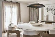 an elegant minimalist dining space with a large white table with a ruffle edge, neutral chairs with plywood frames, a pendant lamp