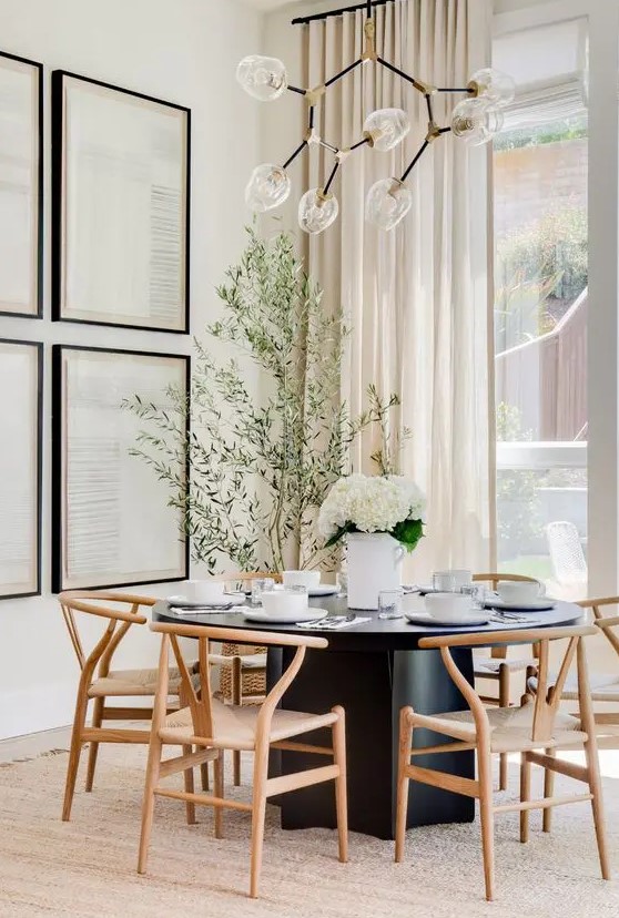 an elegant modern dining space with a black dining table and light-stained chairs, a gallery wall and a catchy chandelier