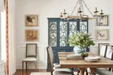 an elegant vintage rustic dining room with a navy buffet, a stained table and matching neutral chairs, a metal chandelier on chain and a gallery wall
