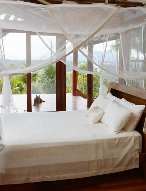 an indoor outdoor bedroom with a bed and neutral bedding, a mosquito net canopy over the bed is a cool idea