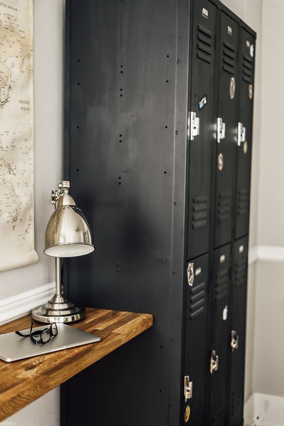 an industrial space with a stack of black lockers for storage, a wall-mounted mini desk, a polished metal lamp and a map on the wall