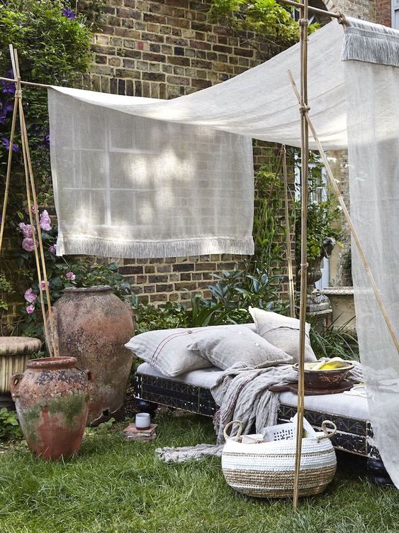 an outdoor bedroom with a vintage bed and grey bedding, a mosquito net canopy, planters with blooms