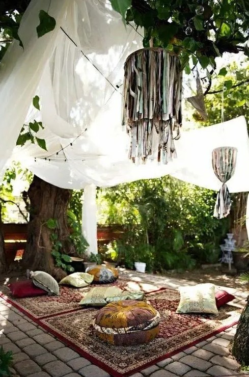 an outdoor boho space done with rugs, pillows, cushions and mosquito nets over it for a mood and vibes more than for bugs