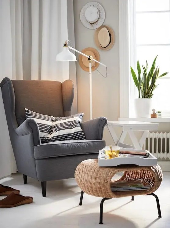 grey Strandmon wing chair by IKEA styled with a striped pillow and with a woven round ottoman is a cool idea for many spaces