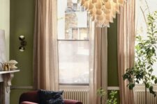 03 a bright living room with olive green walls, a burgundy chair and an orange pouf, a chandelier and blush curtains