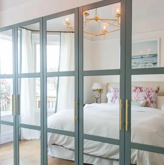 an IKEA Pax wardrobe with fully mirrored front panels with aqua frames and brass handles looks very chic