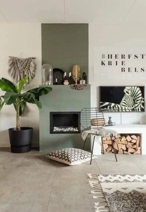 a cool boho nook with an olive green fireplace, a bench with firewood storage, some art and a potted plant