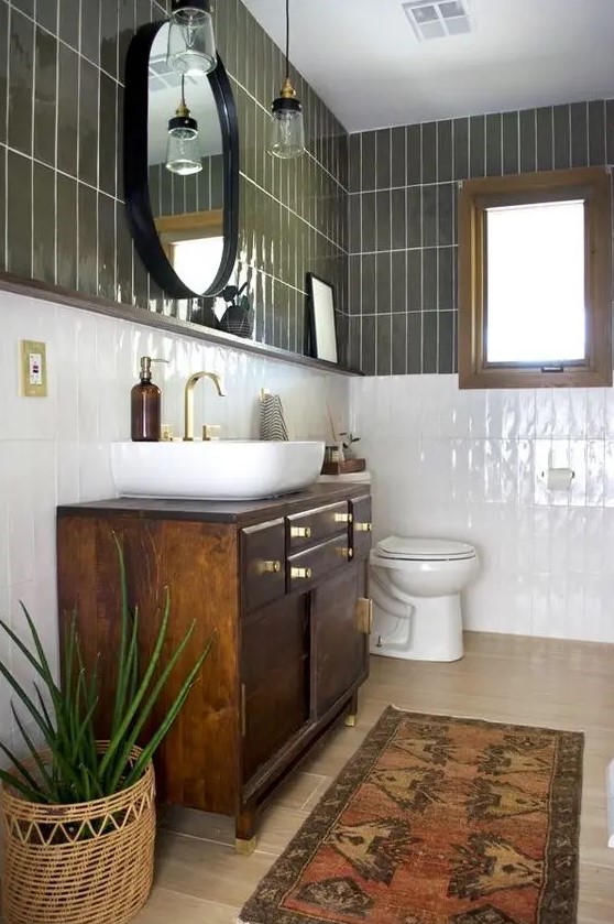 a mid-century modern bathroom with olive green and white skinny tiles, a dark-stained vanity, an oval mirror and a potted plant