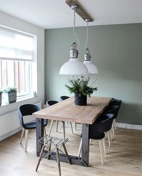 a modern farmhouse dining room with an olive green accent wall, a stained wood dining table, black chairs, white pendant lamp