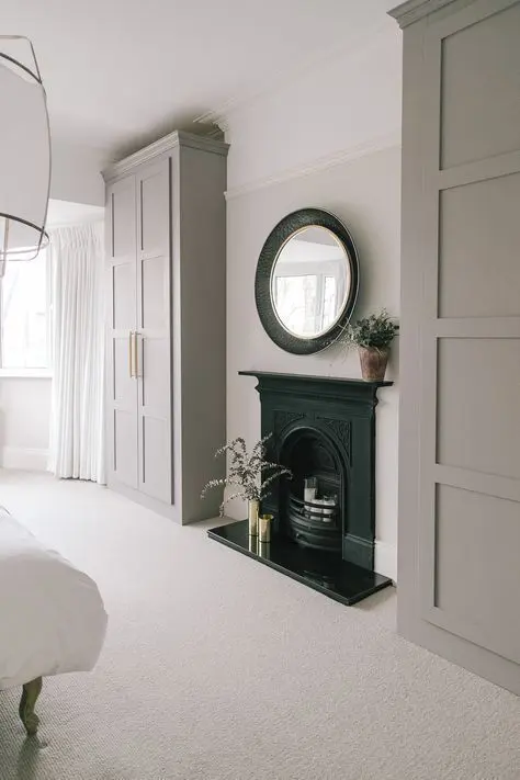 a chic neutral bedroom with a fireplace, two grey IKEA Pax wardrobes and a paper pendant lamp plus some greenery