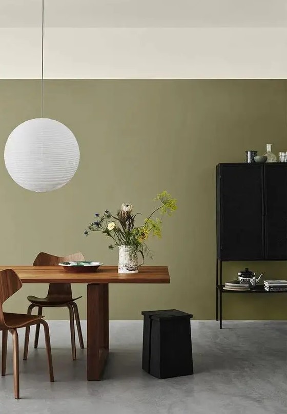 a refined olive green dining room with a stained table and plywood chairs, a black storage unit and a pendant lamp