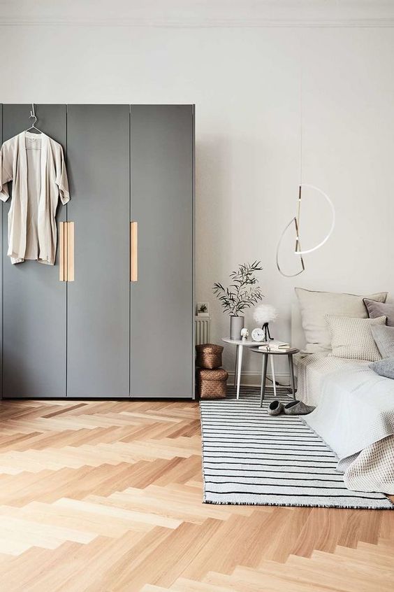 a lovely bedroom with a low bed with neutral bedding, a couple of tables and a rug, a grey IKEA Pax wardrobe