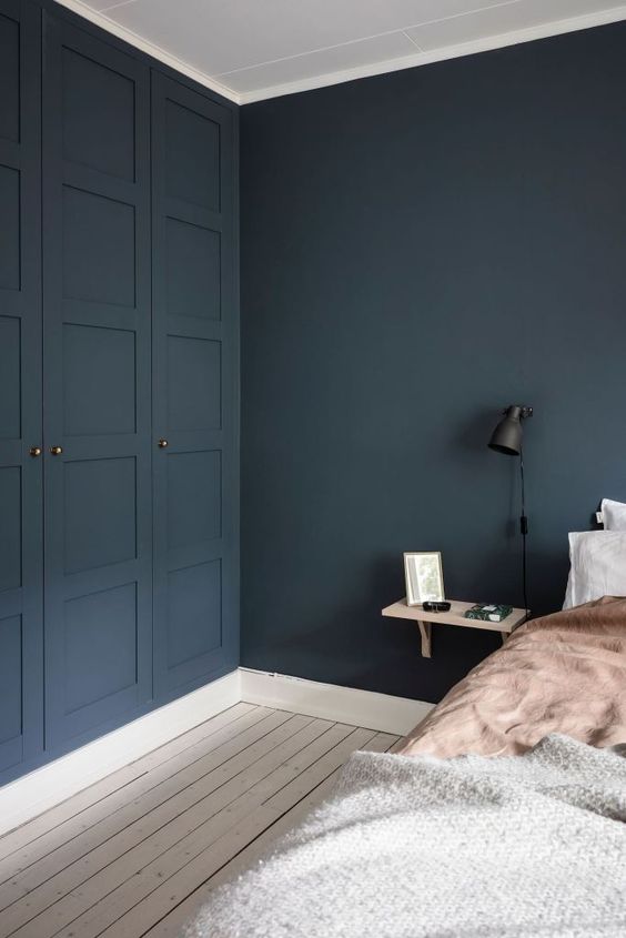 a moody bedroom with navy walls and built-in IKEA Pax wardrobes, a bed with neutral bedding and a floating nightstand