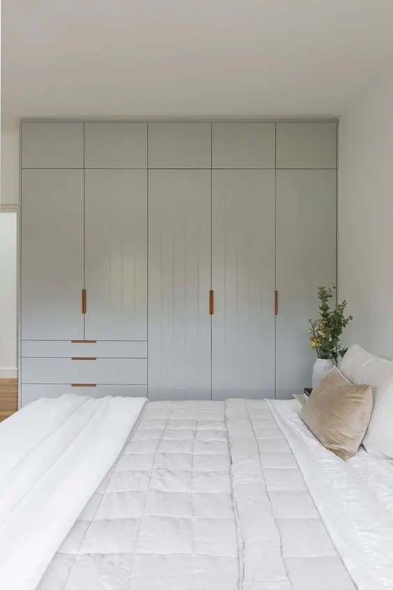 a neutral bedroom with a pale blue wardrobe made of IKEA Pax units and with stained handles, with a large bed and neutral bedding