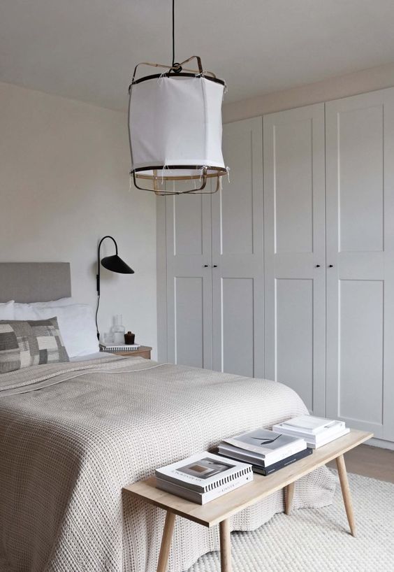 a neutral bedroom with built-in IKEA Pax wardrobes, a grey bed with neutral bedding, a bench and a paper pendant lamp