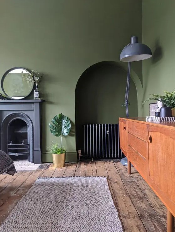 a vintage olive green living room with a non-working fireplace, a niche with a credenza, a stained sideboard, a grey floor lamp and a mirror
