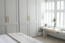 23 a neutral bedroom with dove grey IKEA Pax wardrobes with gold handles, a large bed with neutral bedding, a bench with cool decor